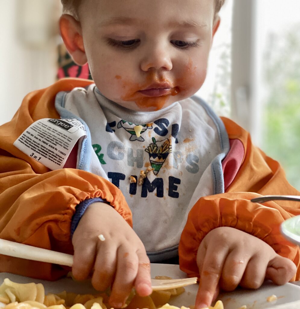 a baby eating pasta with food on his face